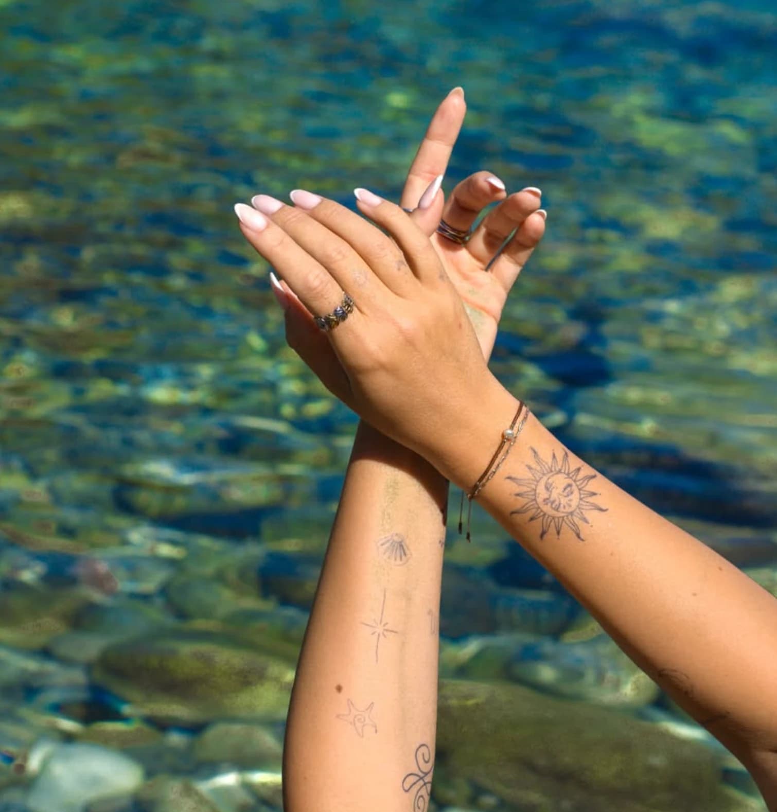 Inkster-Tattoos auf zwei Unterarmen über blaugrünem Wasser